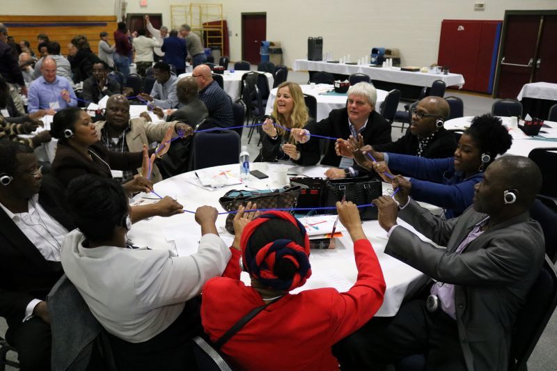 black and white people around a table working on a problem with blue string