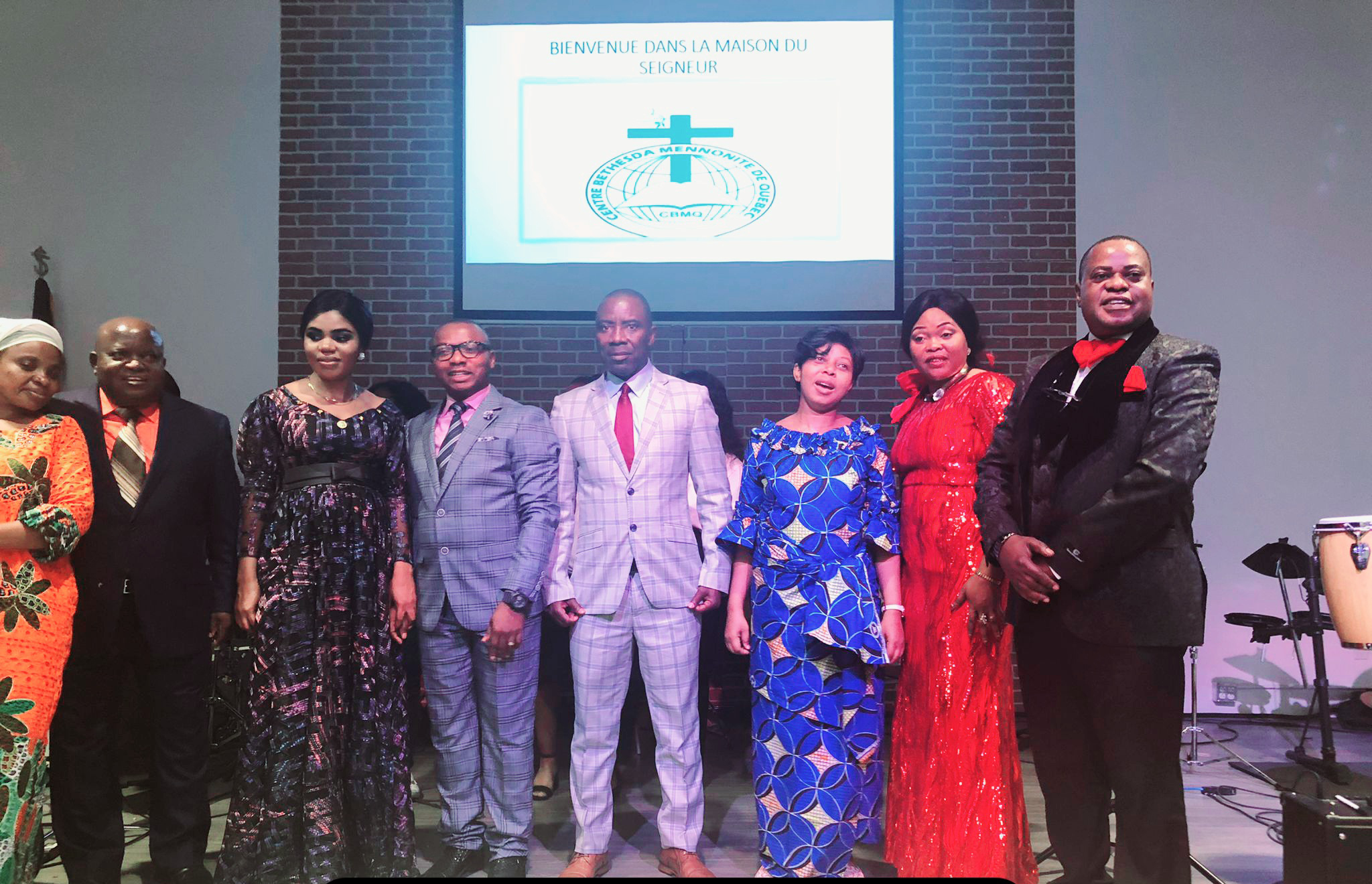 7 men and women standing on stage in colourful dresses and suits