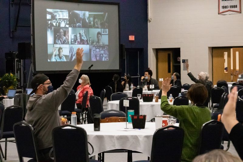 people with hands raised at tables and on screen