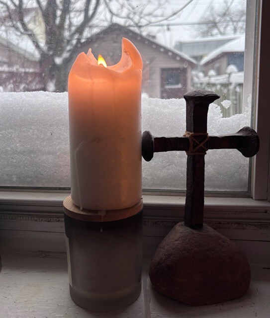 glowing candle and a cross inside a wintry window