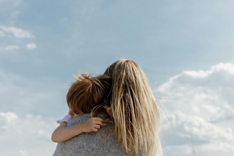 child hugging mom with blue skies and clouds
