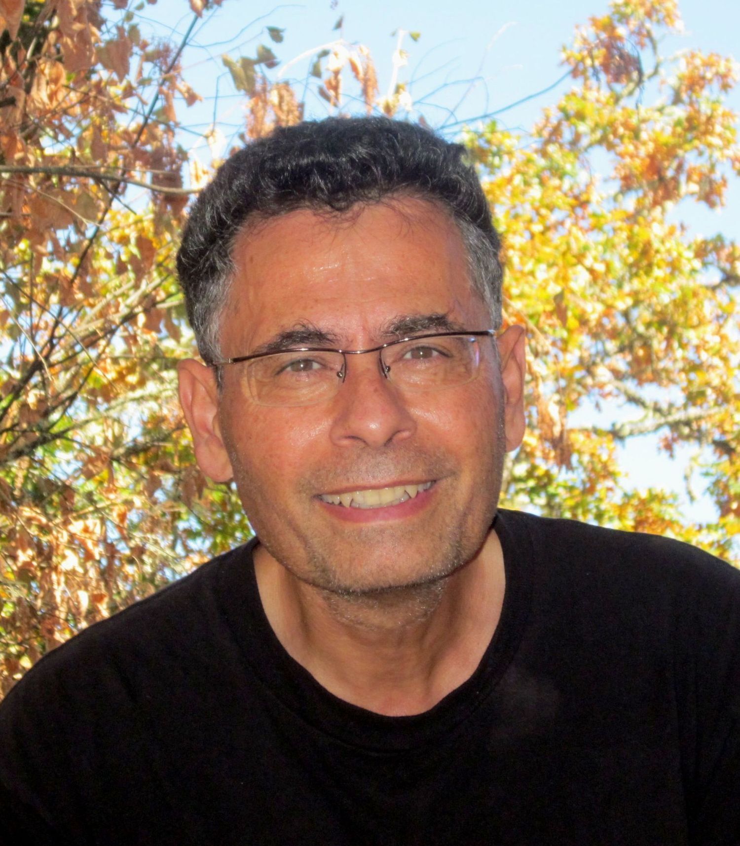 man smiling outside with colourful leaves on tree behind him