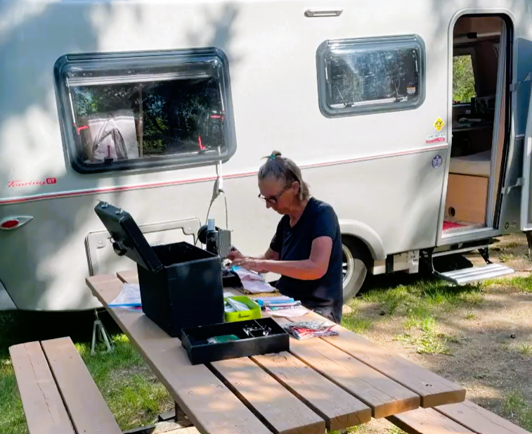 woman sits at sewing machine at campsite
