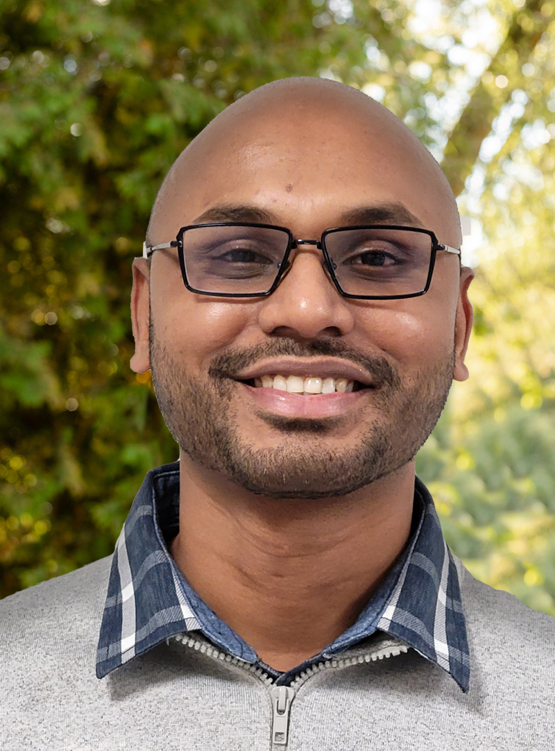 close up image of man smiling outside infront of green leaves of trees