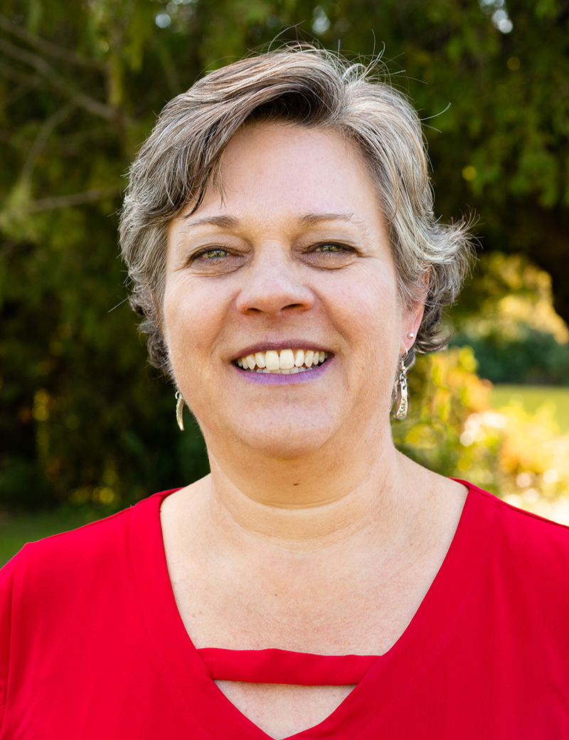 Marilyn Rudy-Froese wearing a red shirt with a tree background