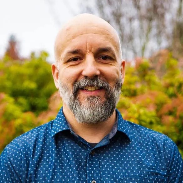 smiling man wearing a blue shirt while standing outside in fall