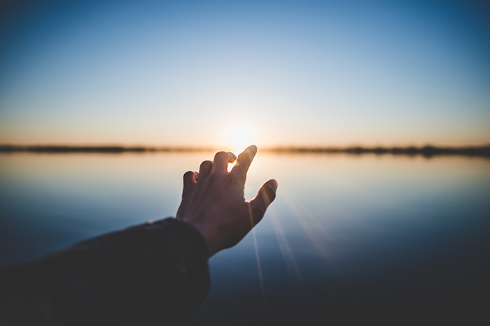 hand reaching to sun on horizon